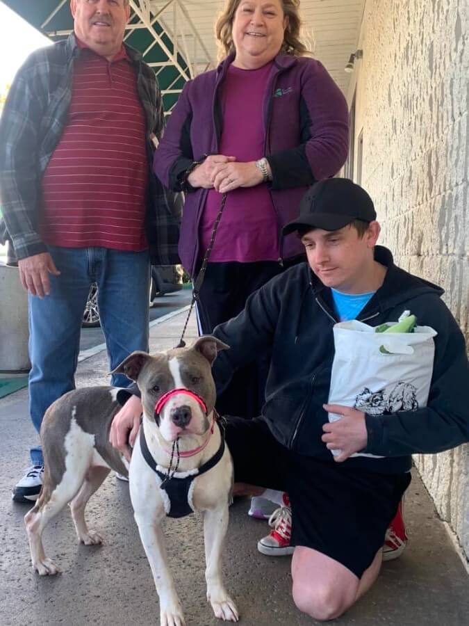 A man and woman pose with a dog in front of a store.