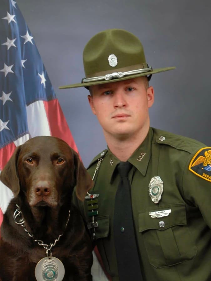 A man in uniform with a dog in front of an american flag.