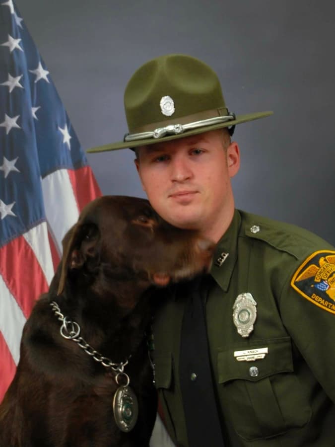 A police officer kisses his dog in front of an american flag.