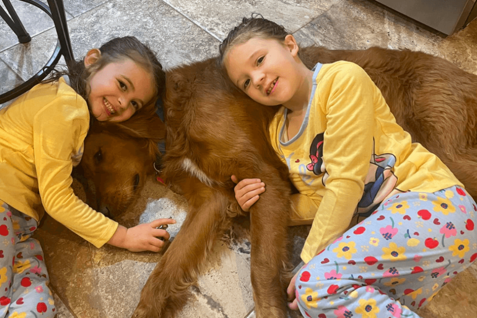 Two girls laying on the floor with a dog.